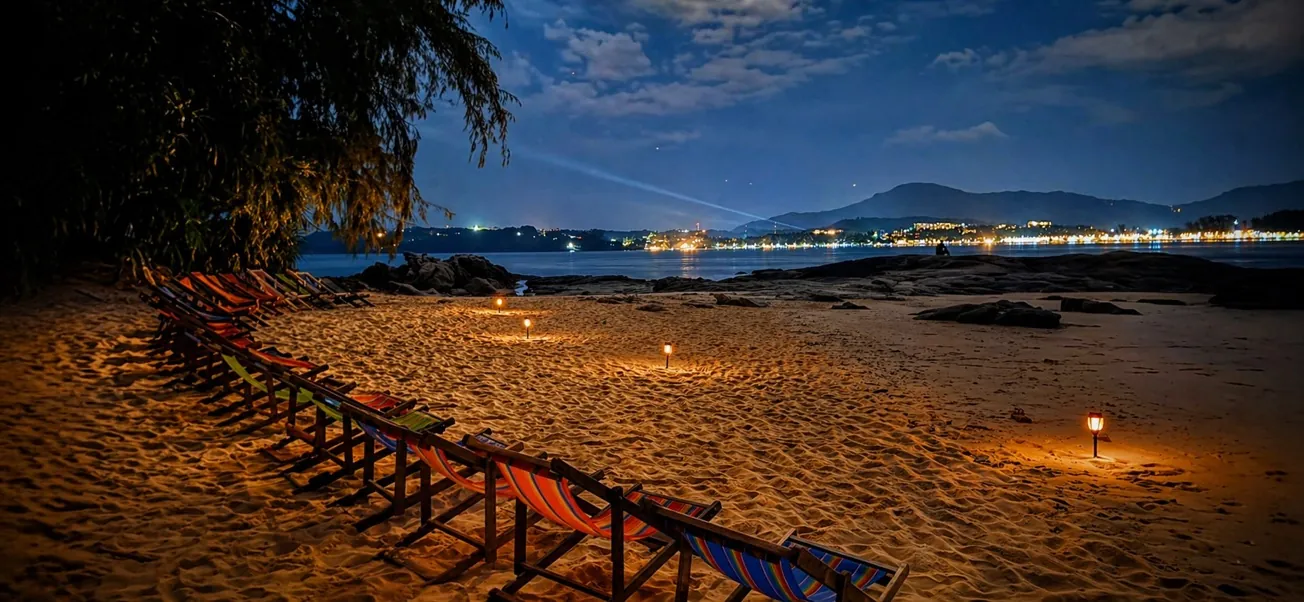 La plage de l’île éclairée aux lanternes à la nuit tombée, face aux lumières de Phuket