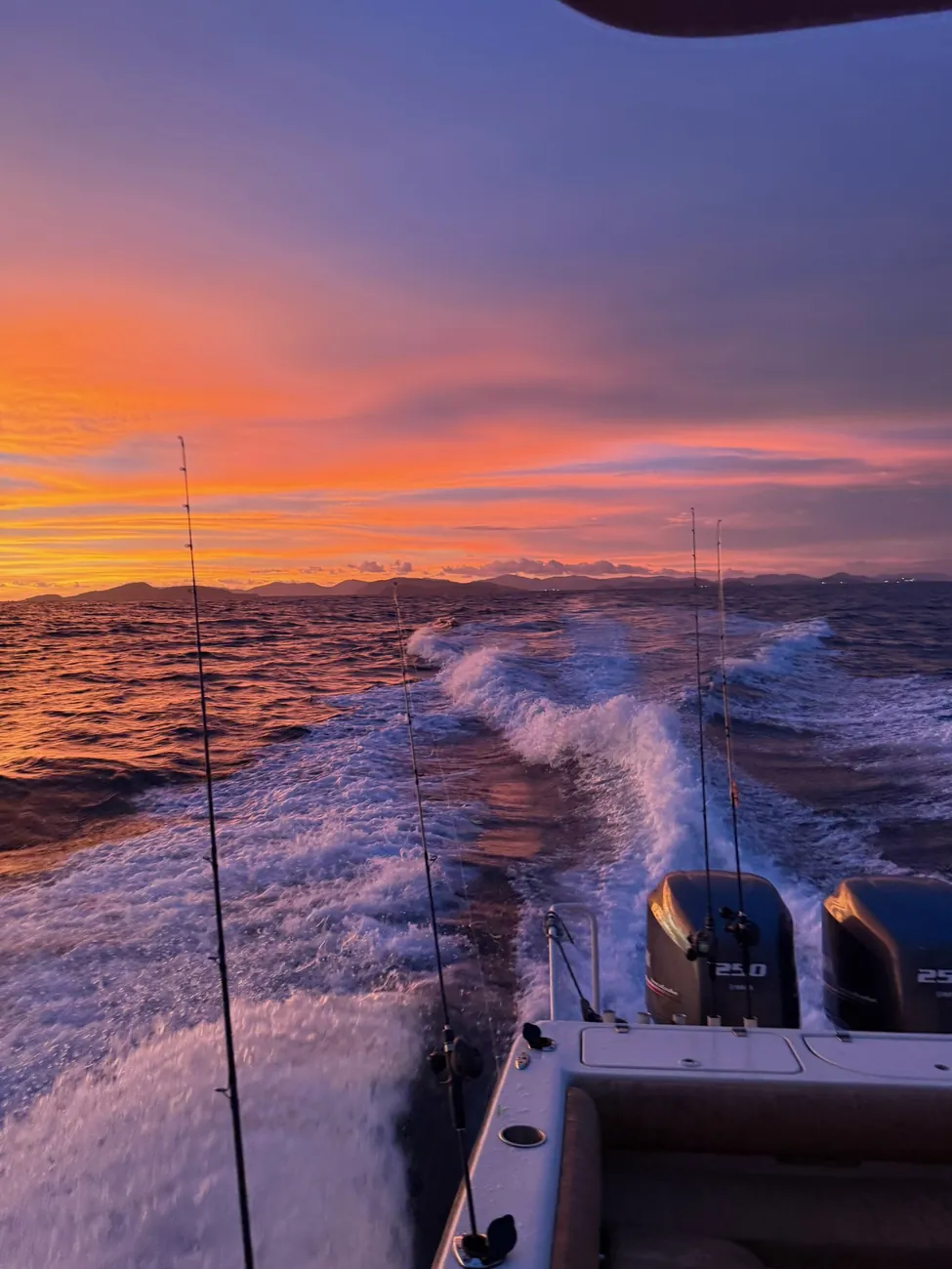 Le sillage du bateau et les cannes à pêche sous un ciel orange au crépuscule