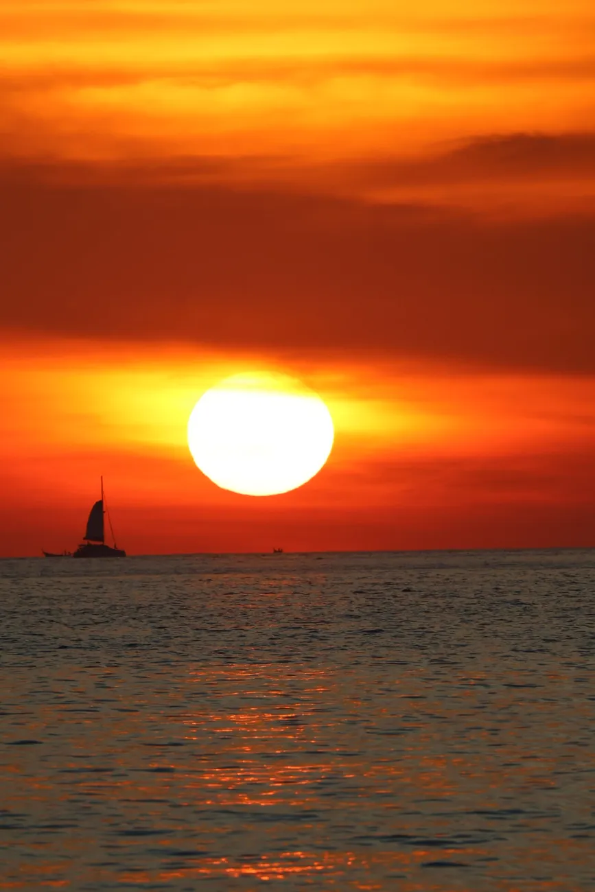 Le soleil plonge dans la mer d’Andaman, un voilier en silhouette à l’horizon